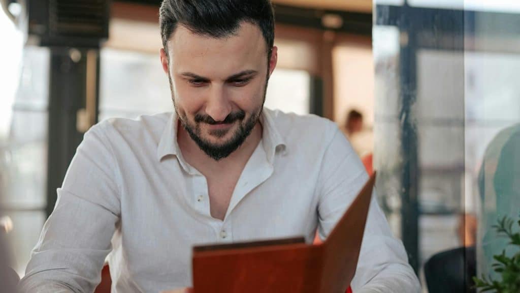 A man smiling while reading a menu at a café table.