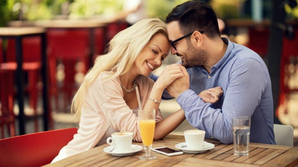 A couple holding hands and smiling together at an outdoor café table.