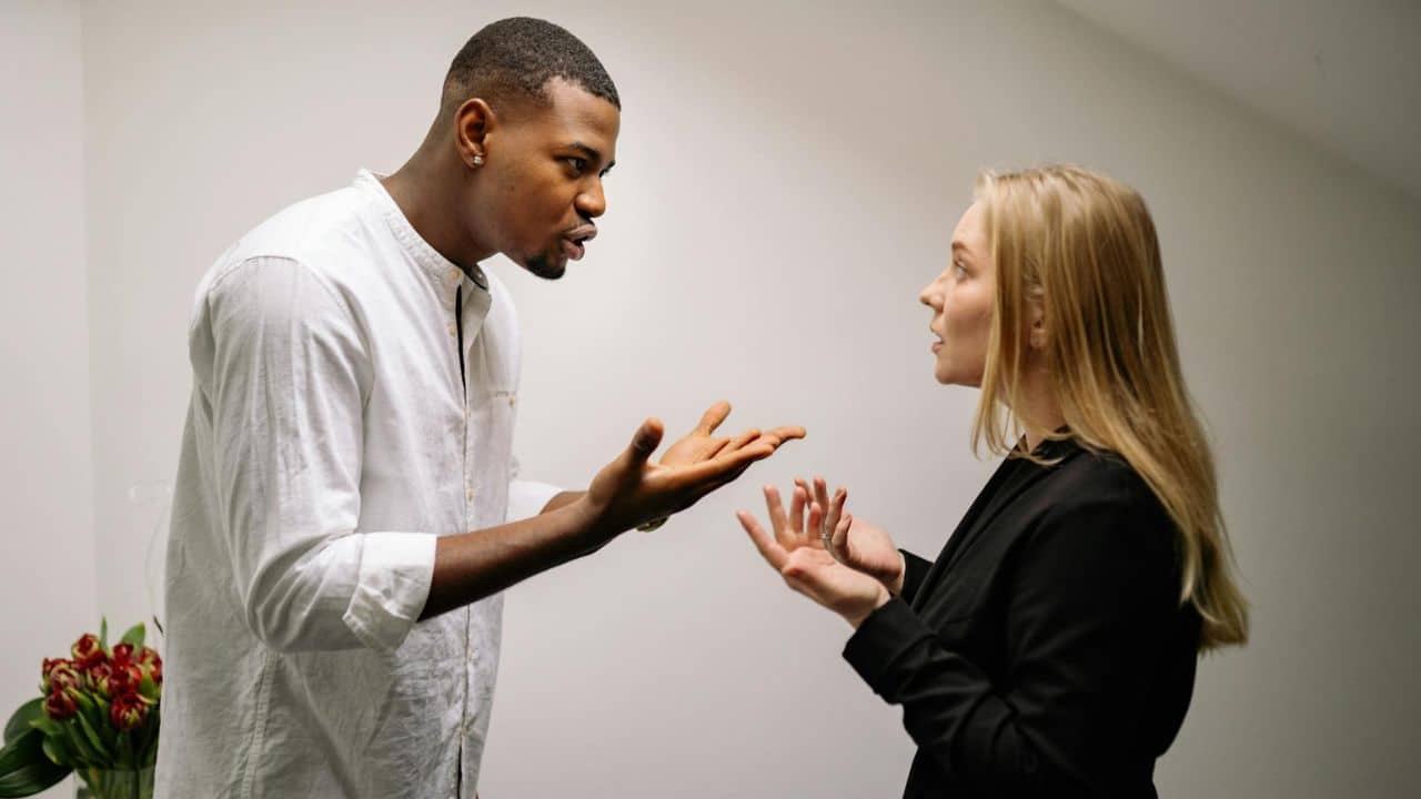 A man in a white shirt and a woman in black gesture during an intense conversation.