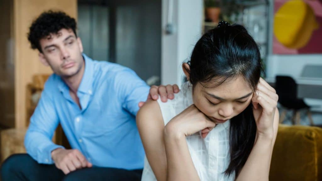 A man in a blue shirt places a hand on the shoulder of a woman.
