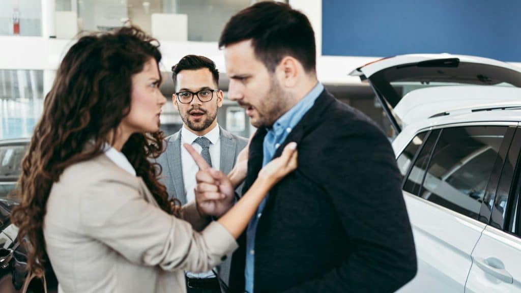A woman grasps a man's lapels and points a finger while another man watches.