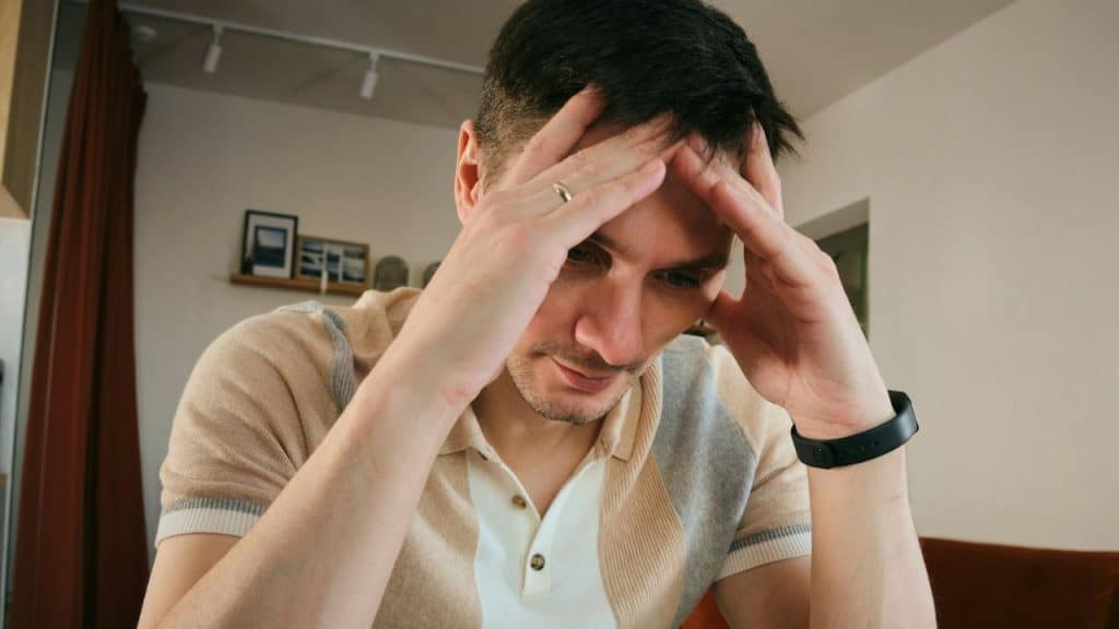 A man in a polo shirt sits with his head resting in his hands, looking down.