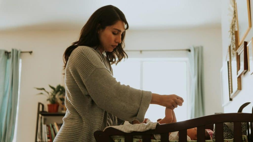 A woman gently changing a baby’s diaper in a crib.