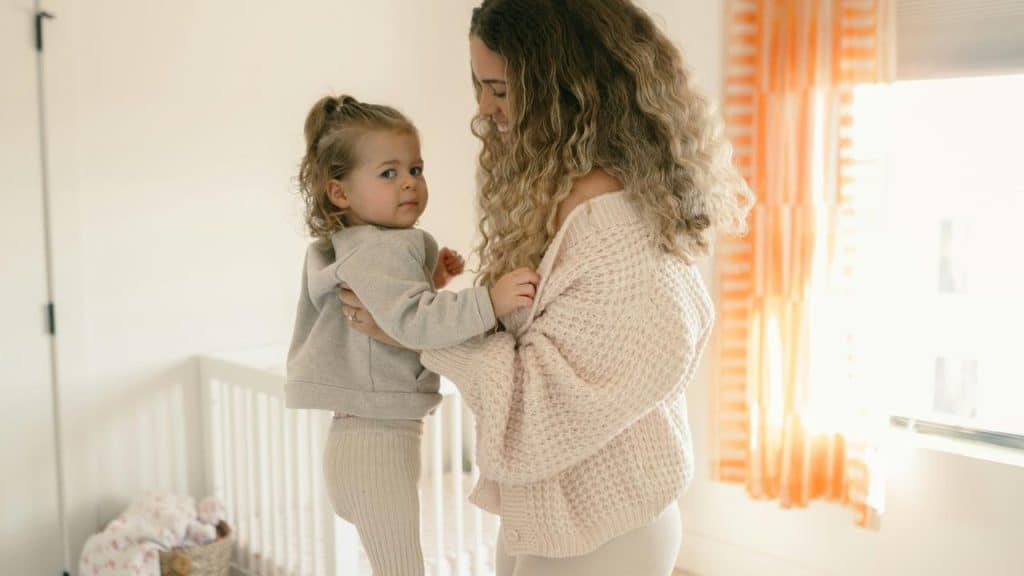 A woman holding a toddler in a softly lit nursery near a crib.