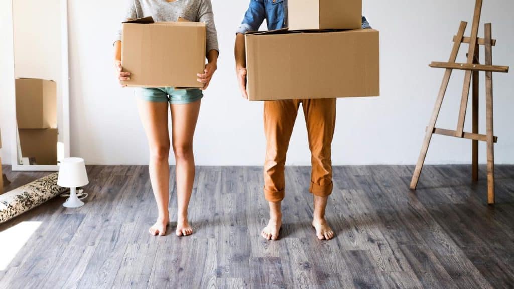 A couple holding cardboard boxes in an empty room.