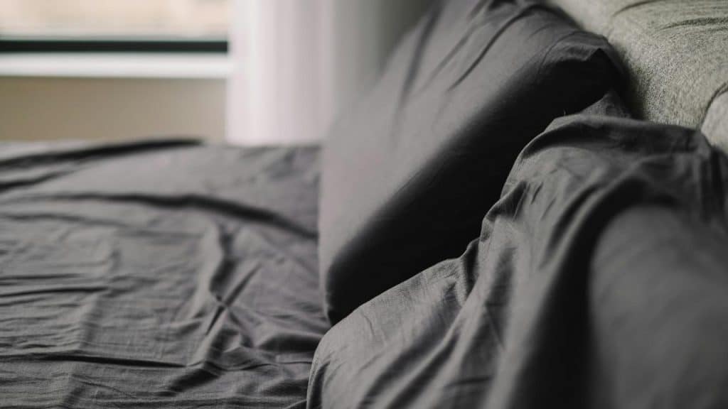 An unmade bed with dark sheets and pillows.