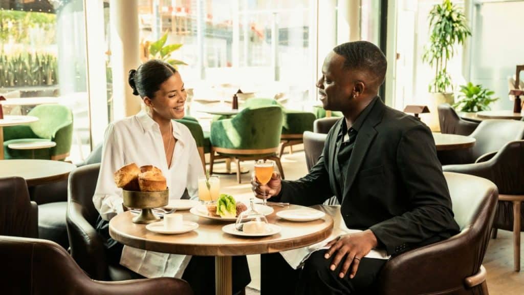 A man and woman sit at a round restaurant table with drinks and small plates.