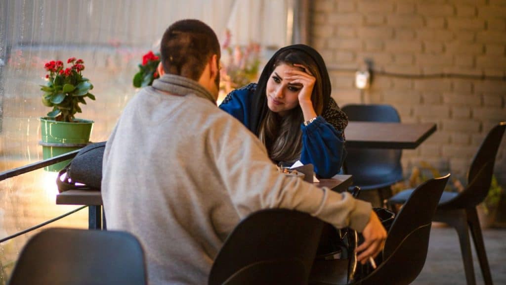 A woman with a headscarf rests her head on her hand while looking at a man.