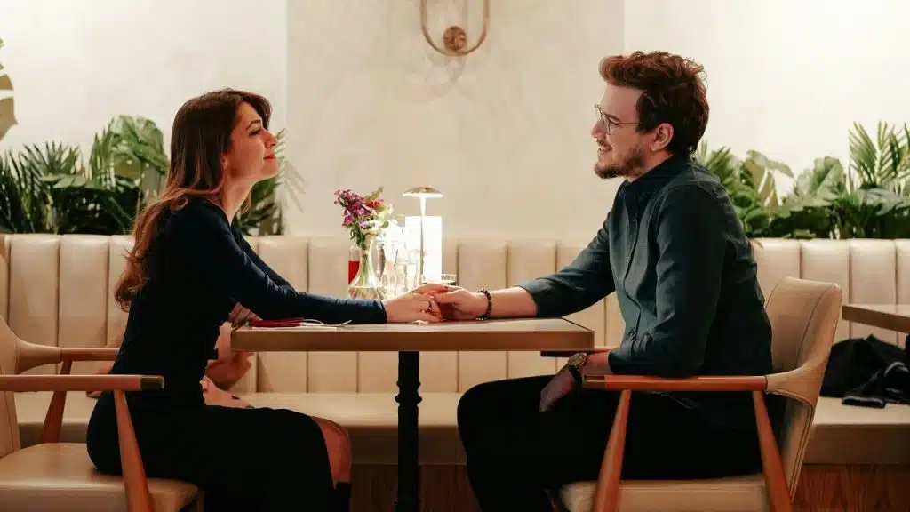 A man and woman sit at a restaurant table holding hands while looking at each other.