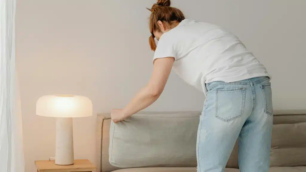 A person adjusting a couch cushion indoors.