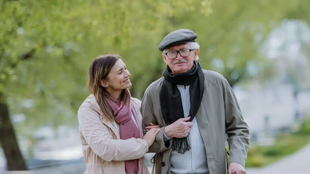 A woman in a pink scarf walks arm-in-arm with an older man wearing a cap.