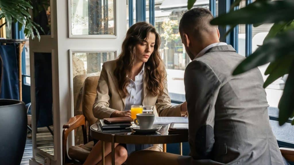 A woman in a tan blazer looks down at papers while sitting at a cafe table.