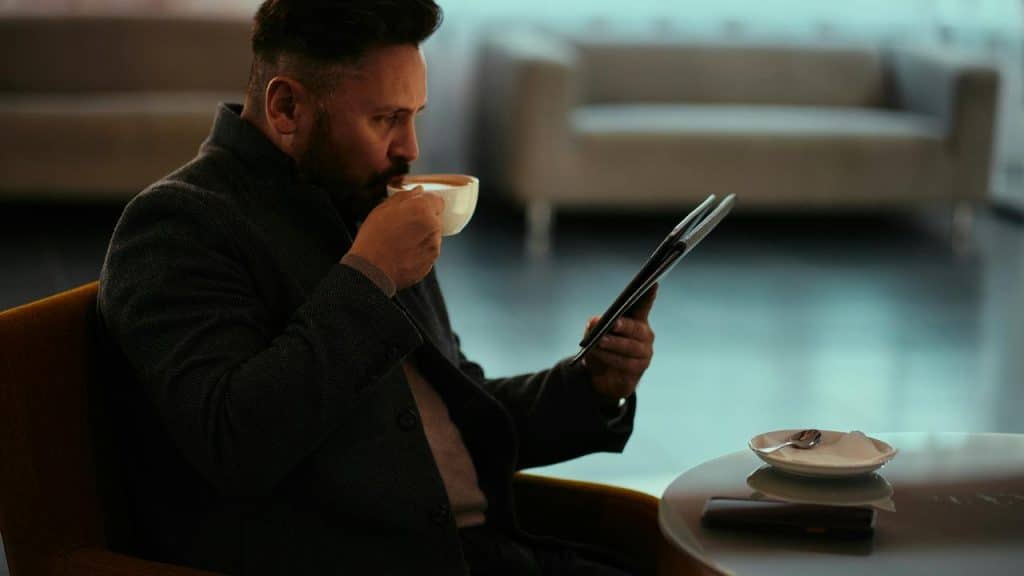 A man drinking coffee while reading a newspaper in a lounge.