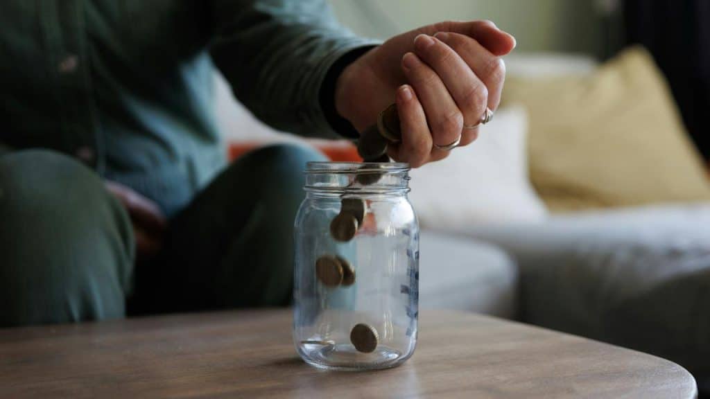 A person dropping coins into a glass jar.