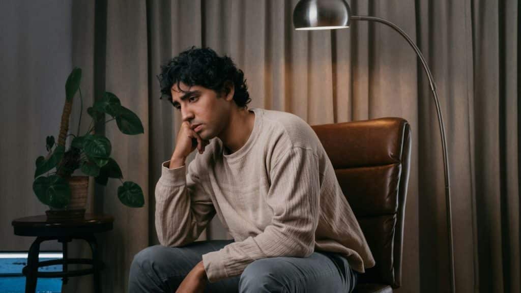 A man sits in a leather chair, resting his chin on his hand with a pensive expression.