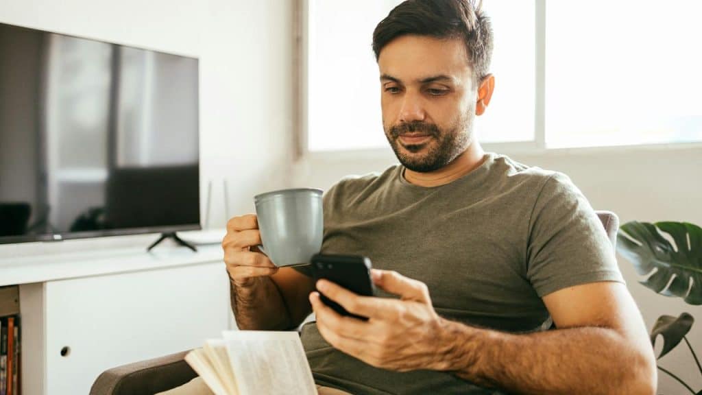 A man sitting with a cup and looking at his phone.