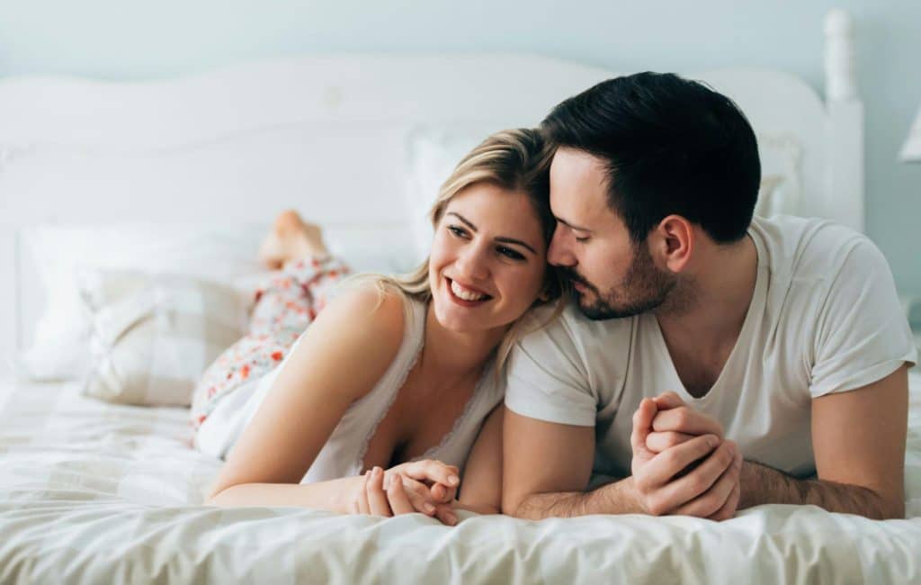 A man and woman lying on a bed while the woman leans against the man’s shoulder.
