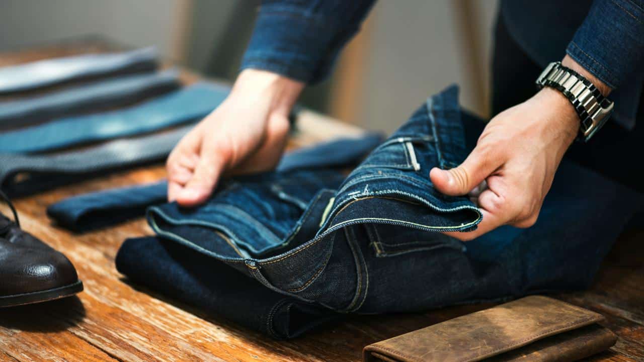 A man folding jeans on a wooden table.