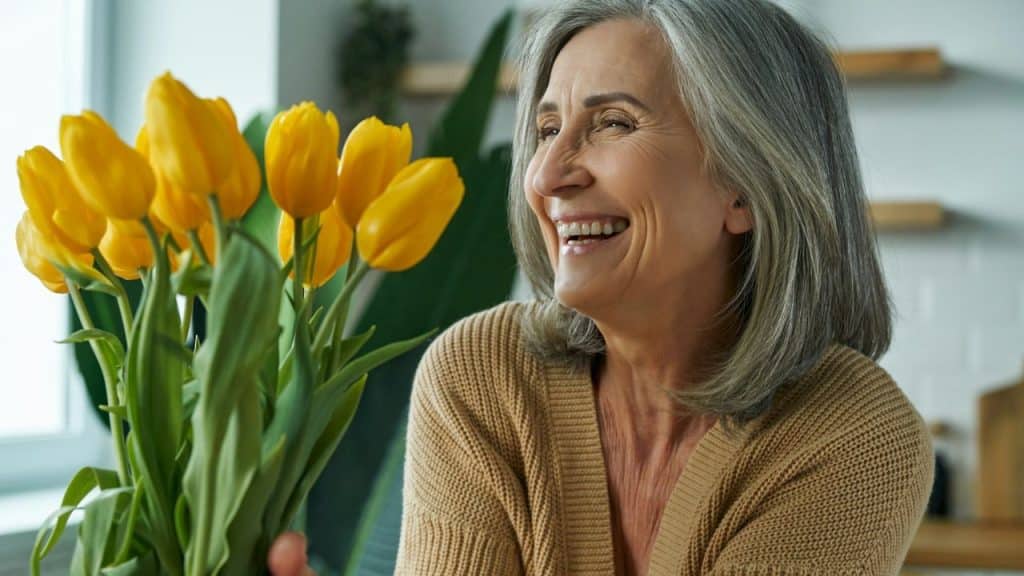 A laughing woman with grey hair looks at a bouquet of yellow tulips.
