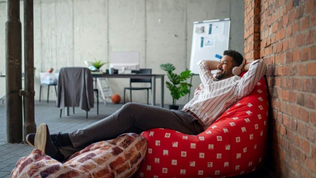A man in a striped shirt reclining in a beanbag chair with headphones on.
