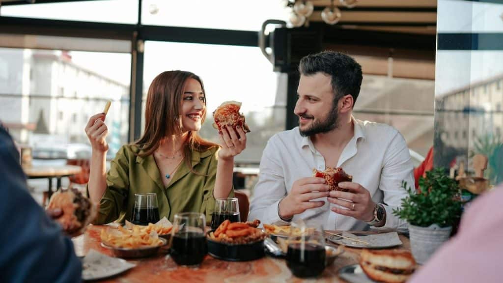 A man and woman sit at a table eating burgers and smiling at each other.