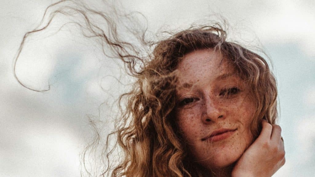 Close-up of a woman with freckles and long wavy hair blowing in the wind.