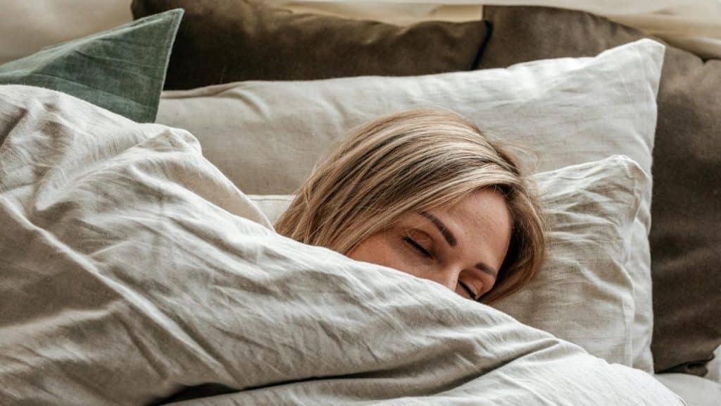 A woman sleeping peacefully under light-colored blankets.