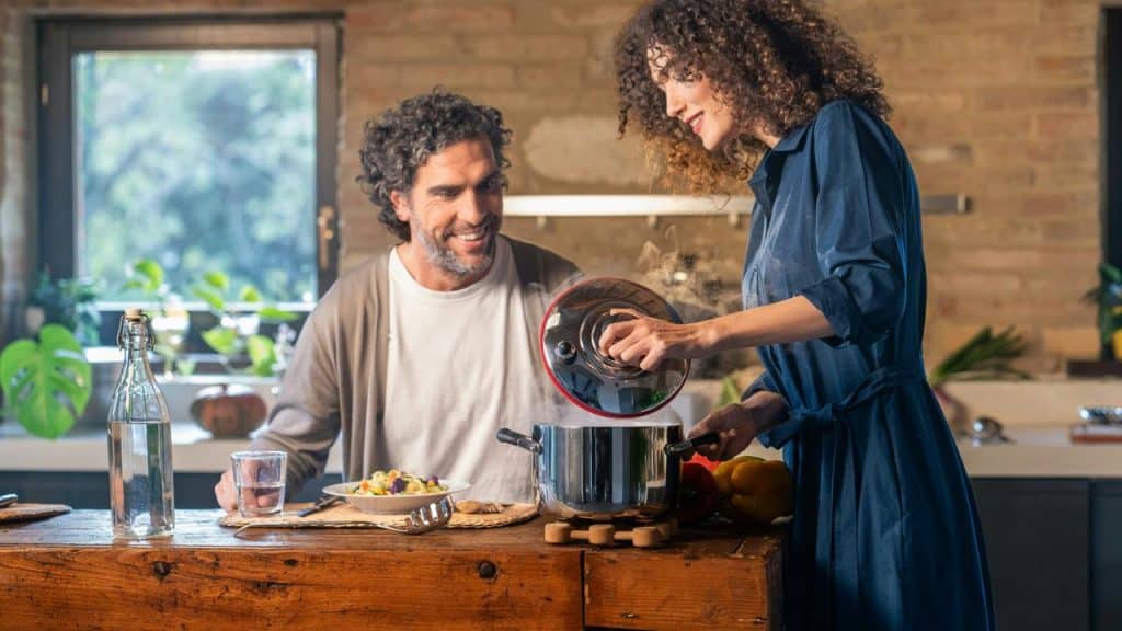 A couple cooking together in a warm kitchen, smiling over a steaming pot.
