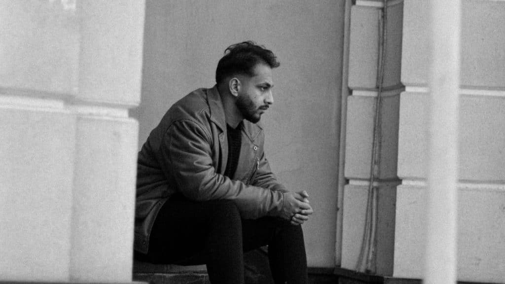 A black and white photo of a man sitting alone on steps with his hands clasped.