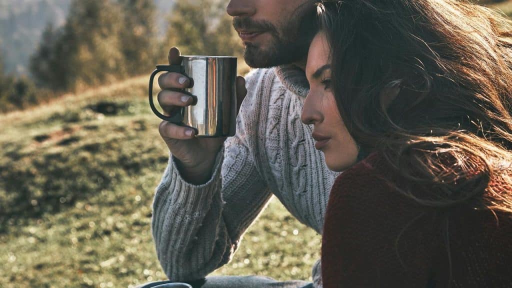 A couple sitting close outdoors, sharing a quiet moment while holding a metal mug.When she lets you in on things she usually keeps tucked away, that’s a strong sign she trusts you. She might drop a quick story about something that shaped her, or tell you what she really thinks about something most people never hear about.
