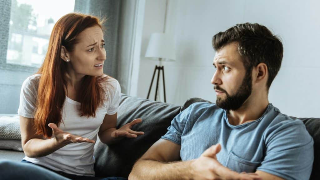 A woman with red hair gestures with her hands while looking at a bearded man.