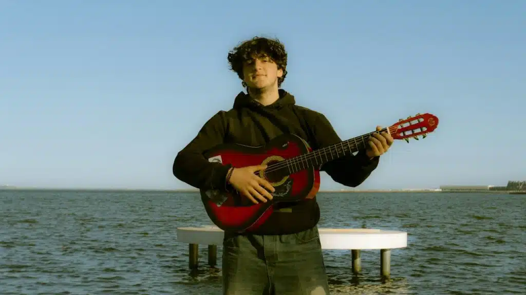 A young man plays guitar near the water.