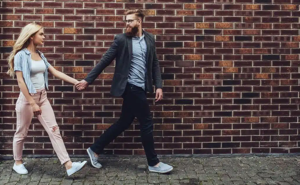 A man holding woman’s hand while walking