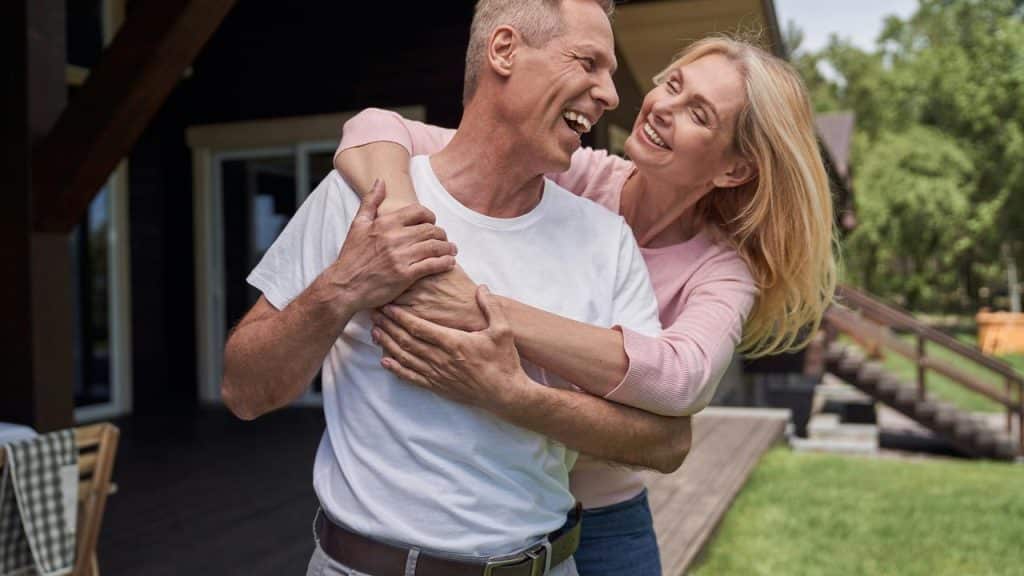 A happy middle-aged woman hugging a laughing man outdoors.