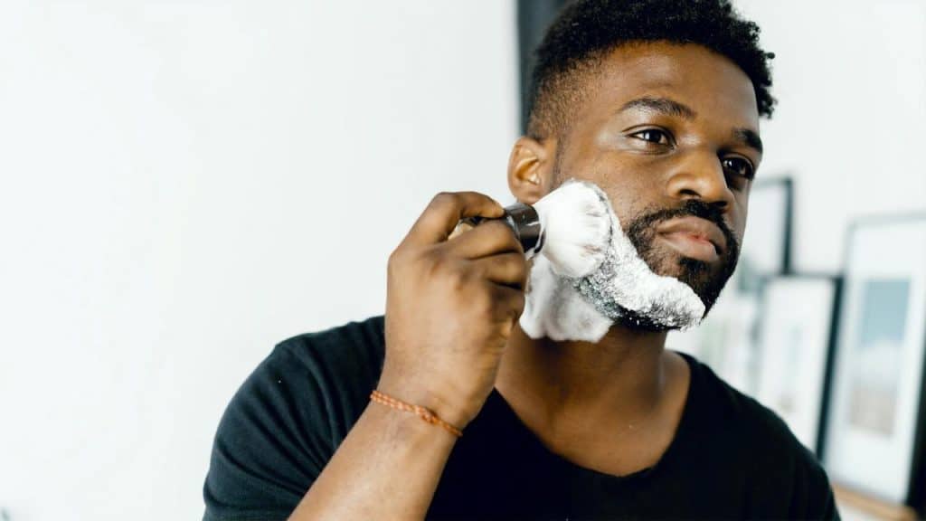 A man using a shaving brush to apply foam to his beard.
