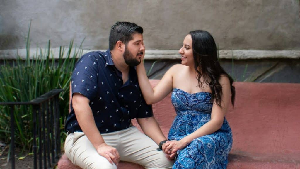 A woman in a blue dress touches a man's face while they hold hands.