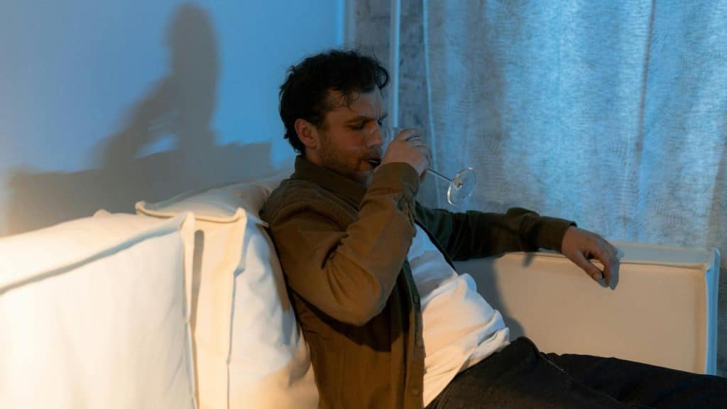 A man sitting on a couch drinking from a glass.