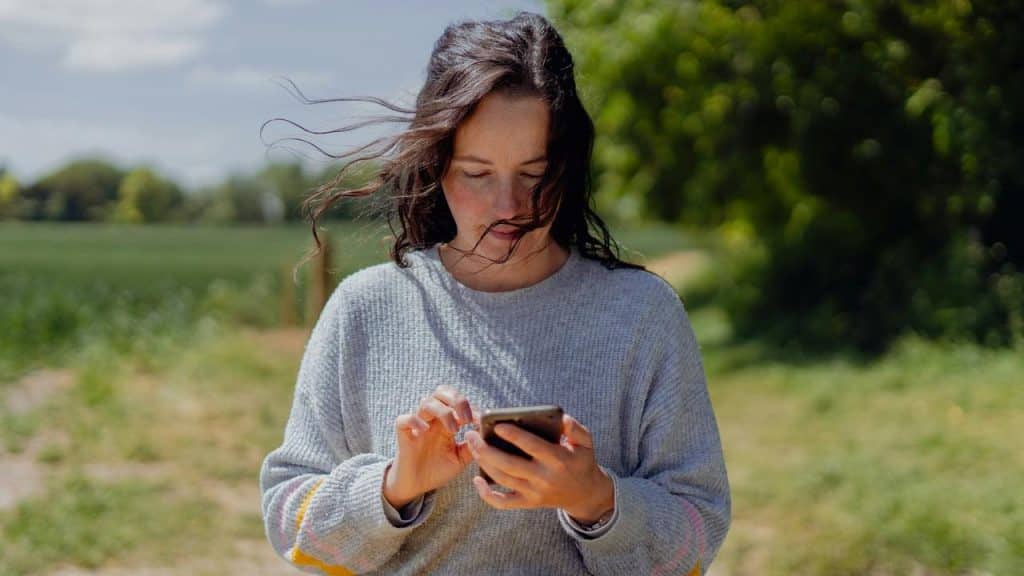 A woman standing outdoors using a smartphone.