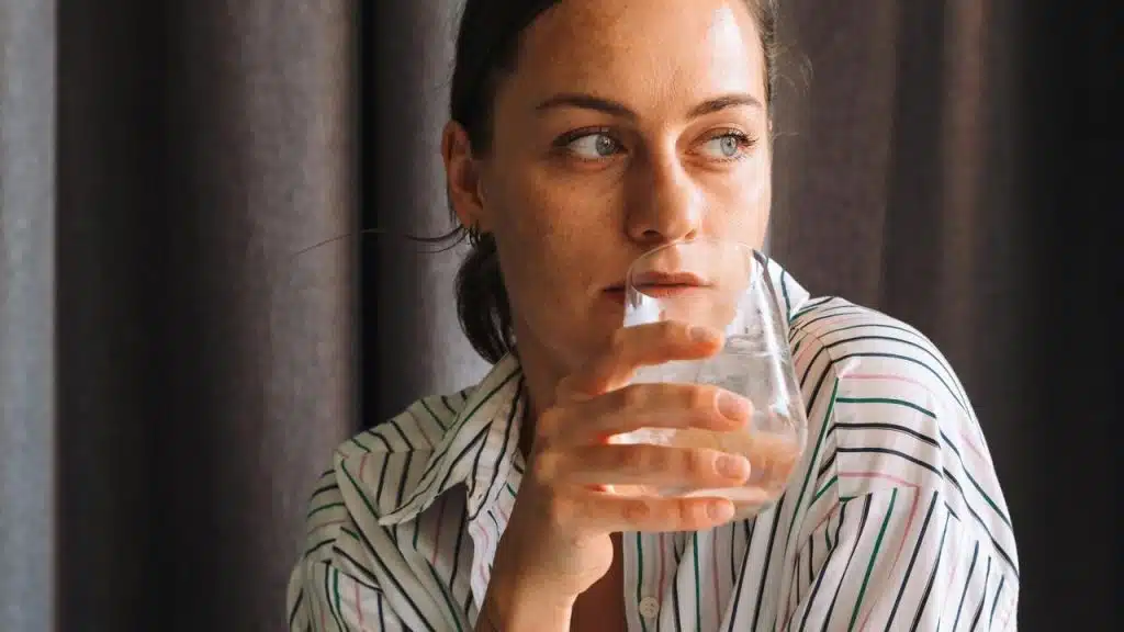 A woman drinks from a glass while looking to the side.