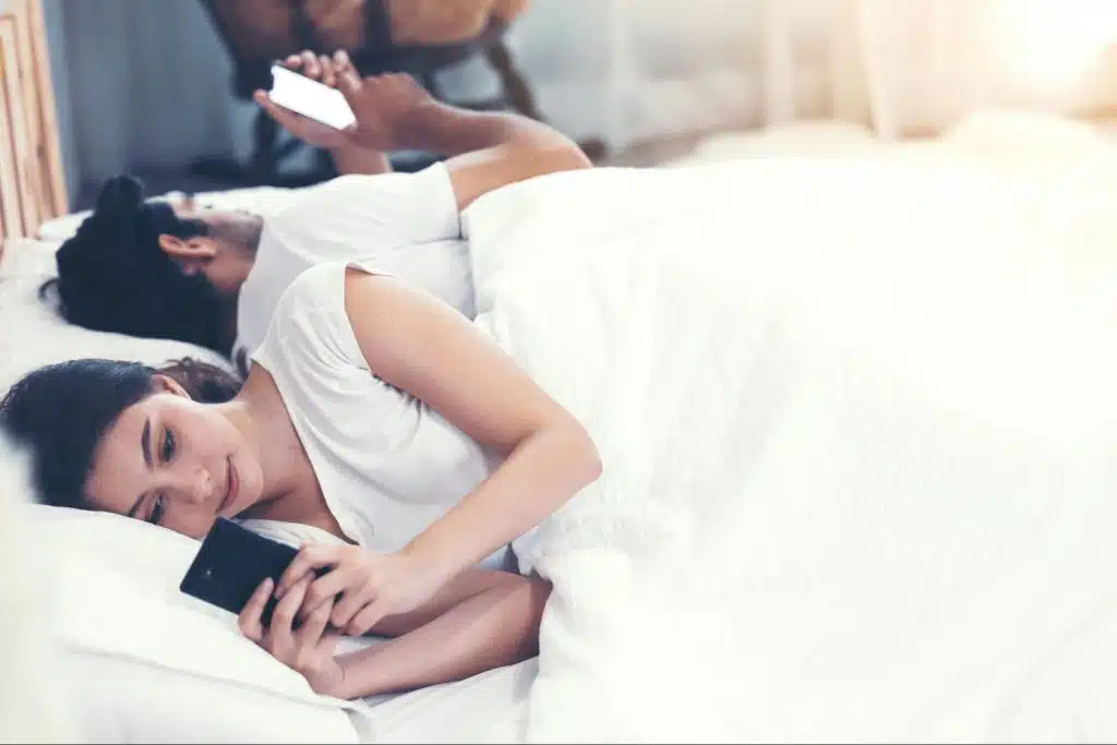 A man and woman using a phone while at the bed 