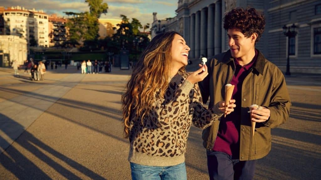 A man and woman walk outside at sunset while laughing and holding ice cream.