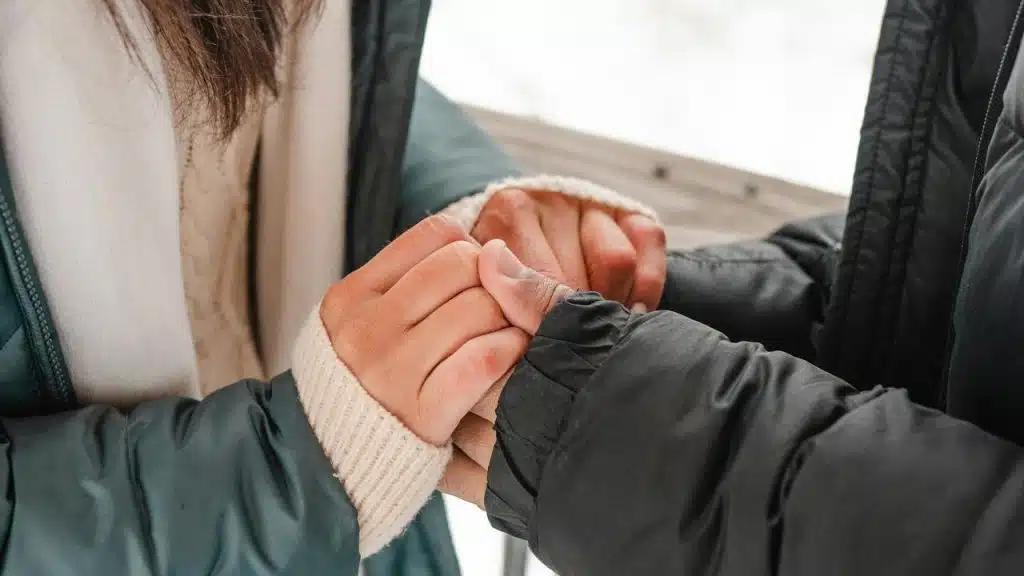 A close-up of two people holding hands while wearing winter jackets.