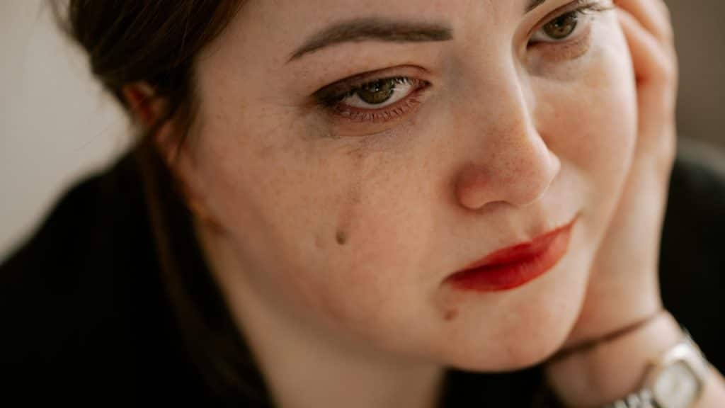 A woman is crying with her mascara running down her cheek because of it.