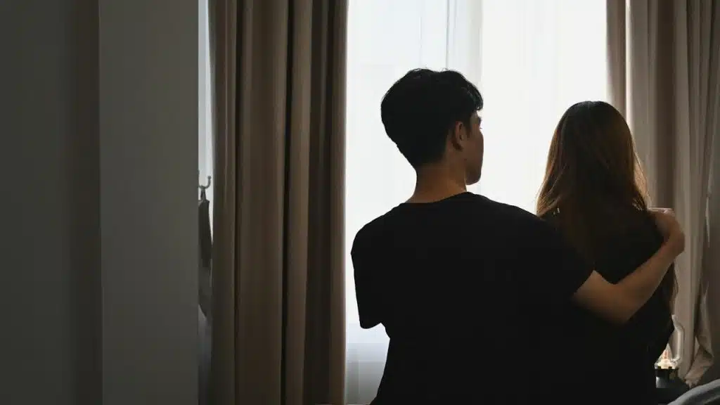 Back view of husband holding his angry wife in the bedroom.