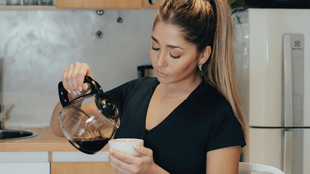 A woman with her hair in a ponytail pours coffee from a glass pot.
