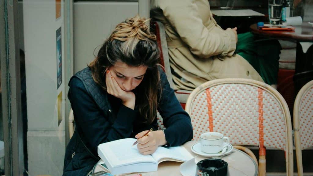 A woman reading and taking notes at an outdoor café table.