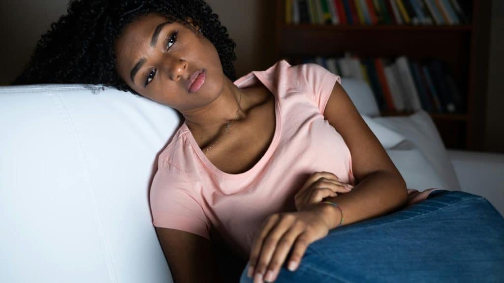 A woman lying on a couch with a pensive expression, gazing off to the side.