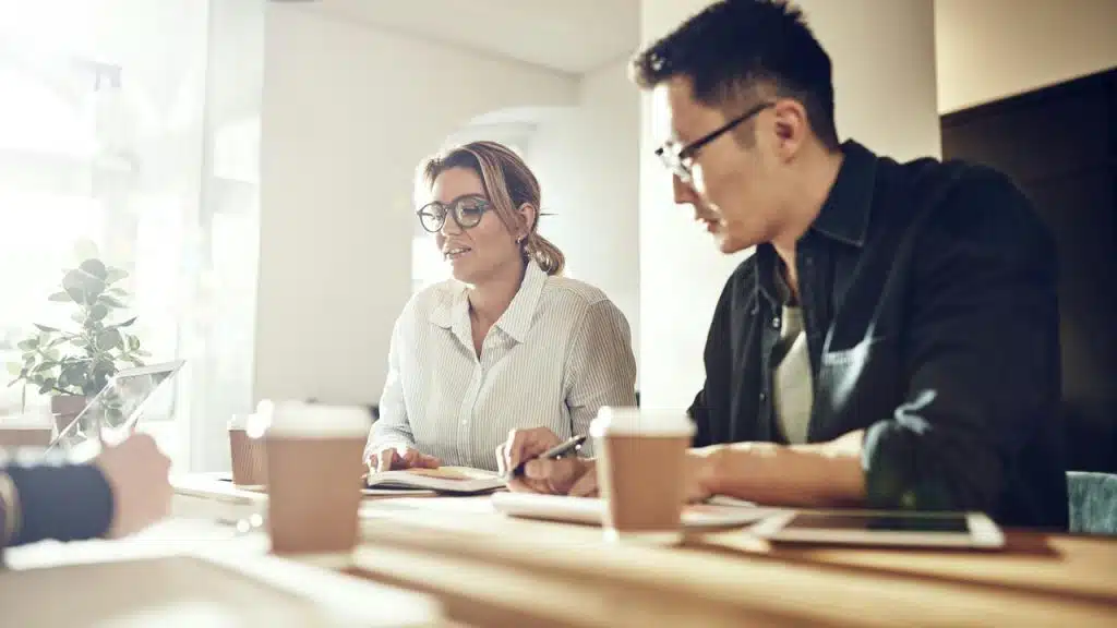 A group of coworkers discussing ideas around a table with notebooks and coffee cups.