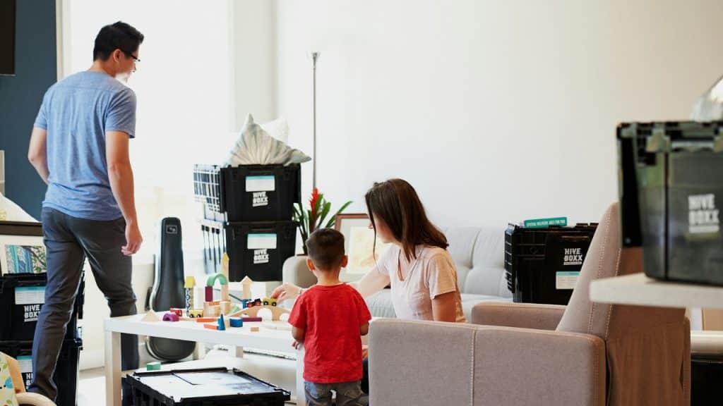 A woman and child play with blocks on a table while a man walks away.