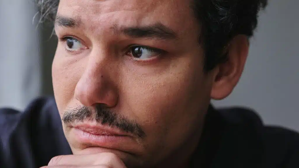 A close-up of a man with a mustache looking off-camera with a concerned expression.